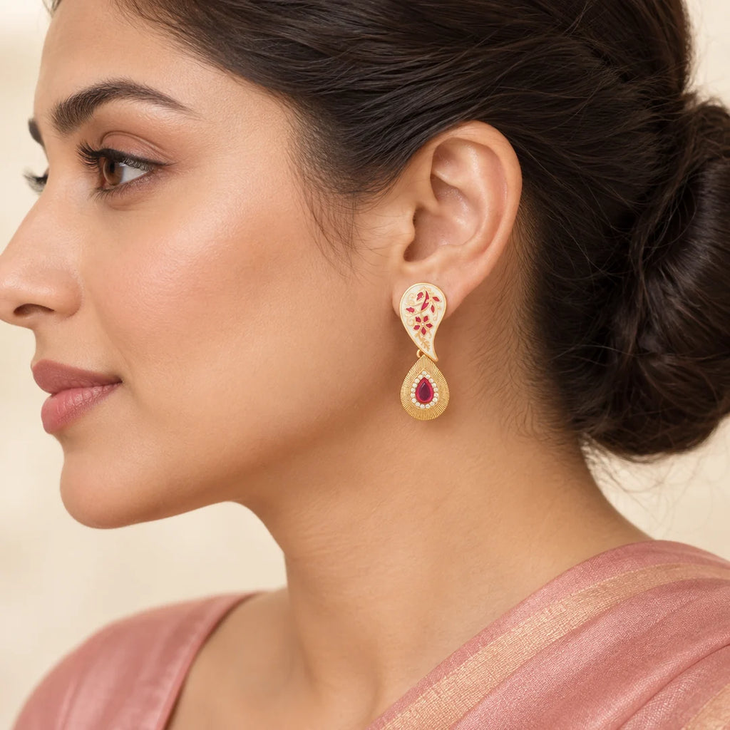 Model in side profile wearing a single ivory and ruby-pink Pallavi paisley earring with a gold-tone teardrop pendant.