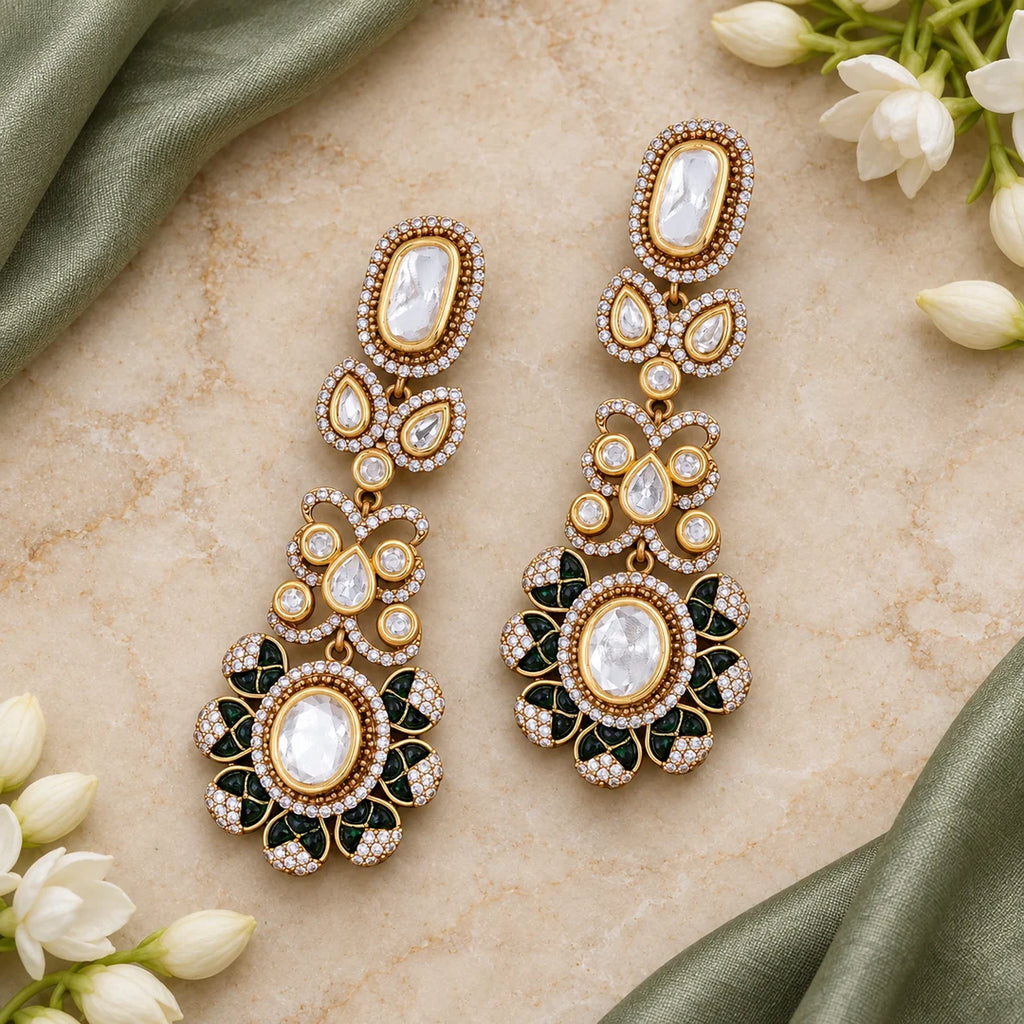 Pair of clear and green long drop earrings lying flat on ivory stone beside sage silk and white jasmine.