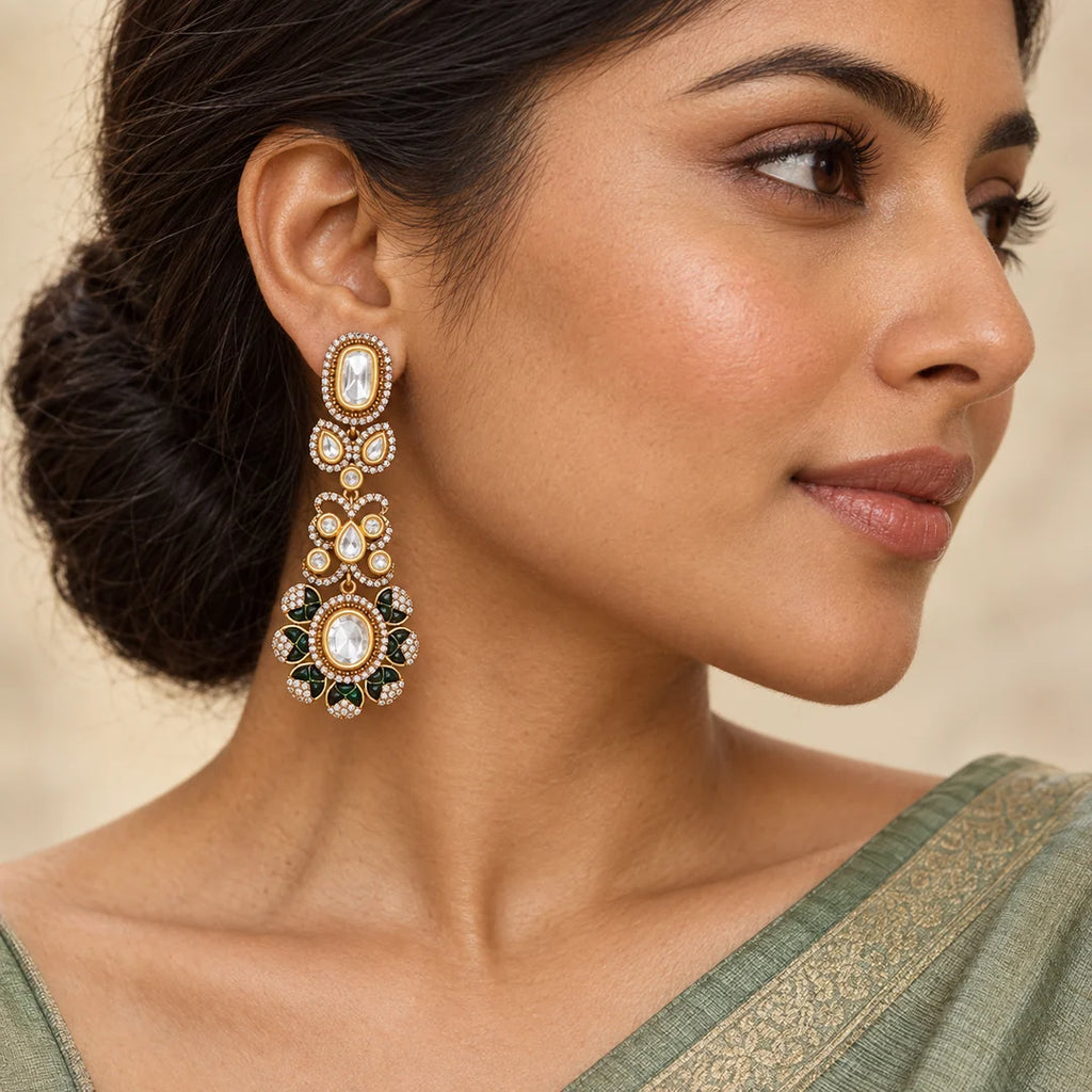 Close-up of an Indian model in a sage saree wearing a long gold-tone earring with clear stones and dark-green floral accents.