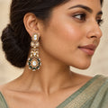 Close-up of an Indian model in a sage saree wearing a long gold-tone earring with clear stones and dark-green floral accents.