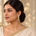 Indian model in an ivory saree wearing long gold-tone earrings with clear stones and ruby-coloured centres surrounded by green floral accents.