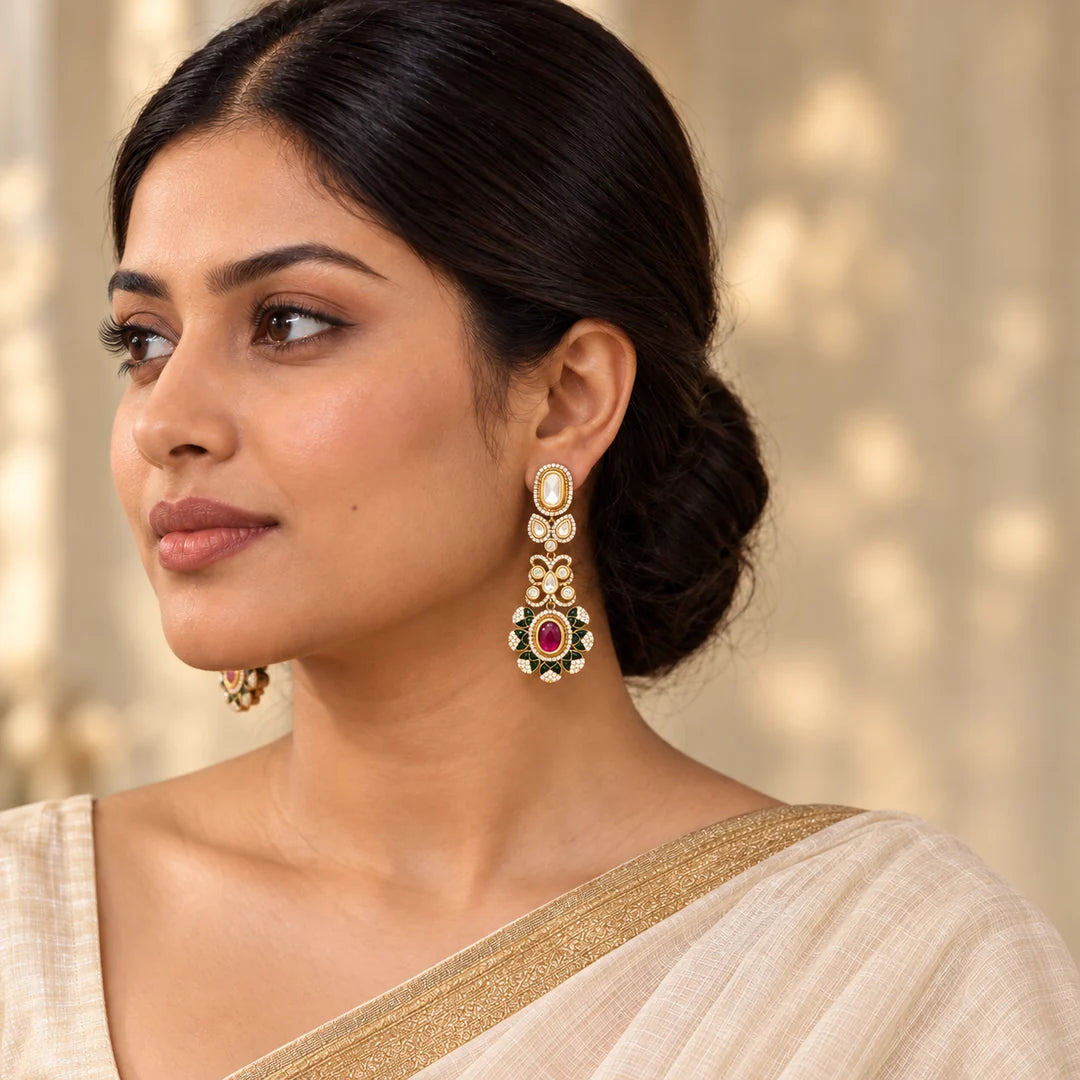 Indian model in an ivory saree wearing long gold-tone earrings with clear stones and ruby-coloured centres surrounded by green floral accents.