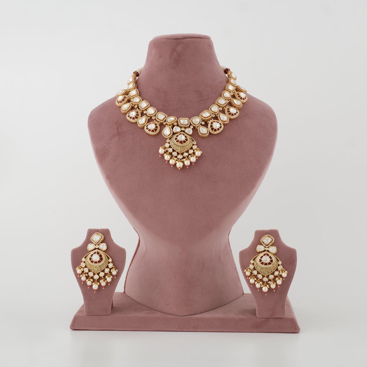 Gold-toned traditional jewelry set displayed on a dusty rose velvet mannequin bust, including a statement necklace and matching earrings.