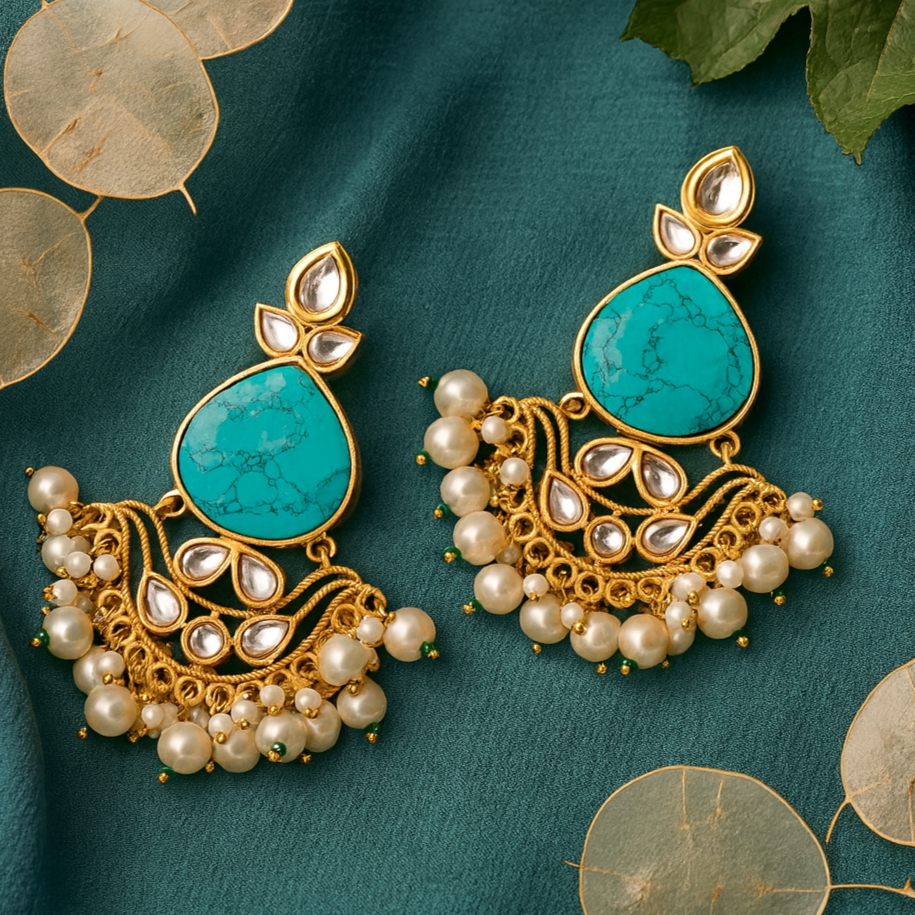 Ornate earrings with turquoise stones and pearl accents on a teal fabric background.