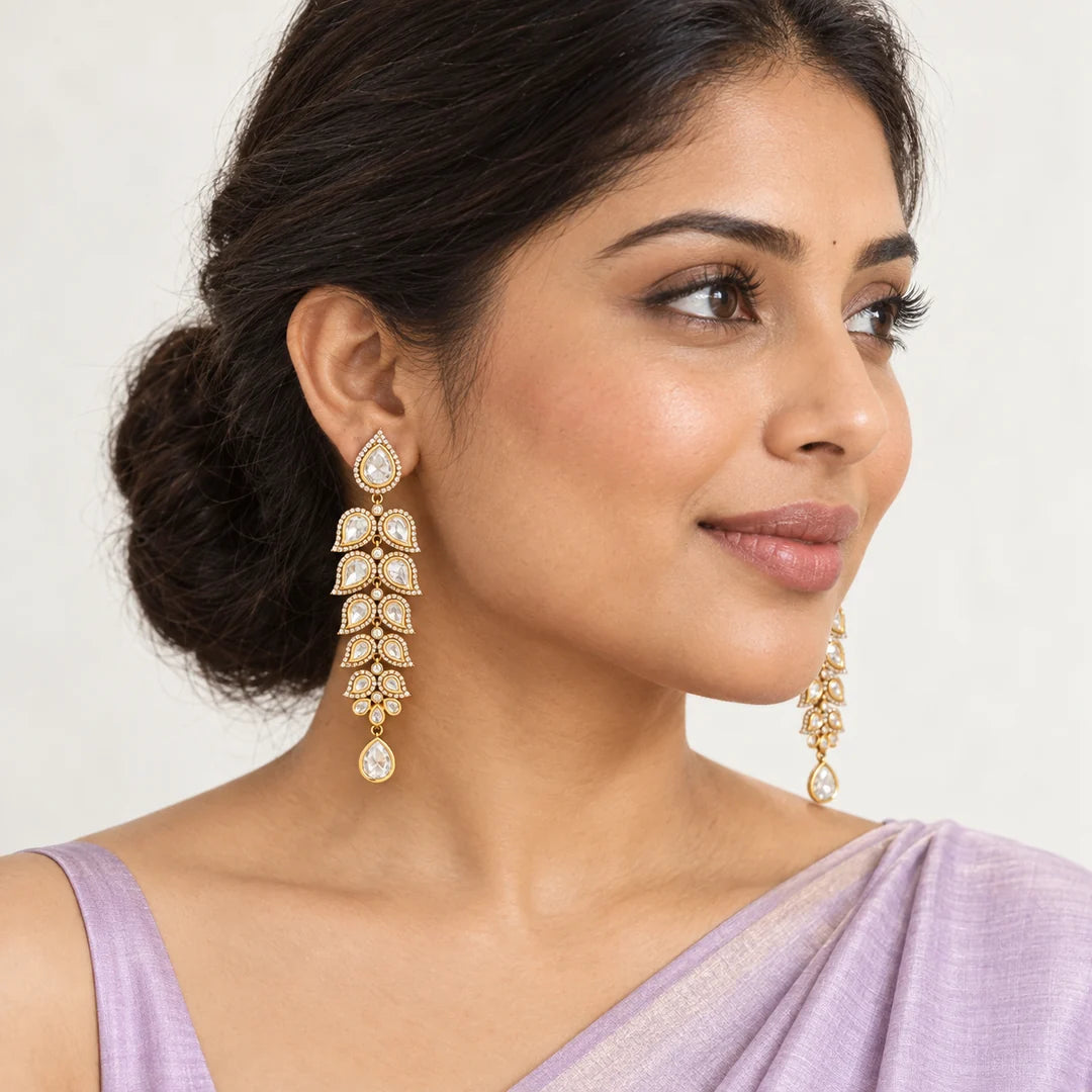 Indian model in a lavender saree wearing long clear-stone leaf earrings with gold-tone settings and teardrop finishes.