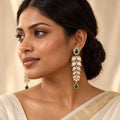 Indian model in an ivory saree wearing long leaf earrings with clear stones, green teardrop tops and matching green drops.